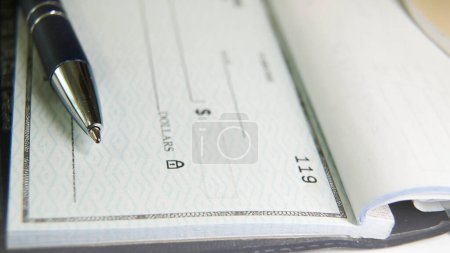Téléchargez les photos : Un stylo bleu est placé sur un chèque en blanc avec sa pointe reposant près de la ligne de montant du paiement, prêt à ce que quelqu'un remplisse les détails nécessaires pour une transaction financière. - en image libre de droit