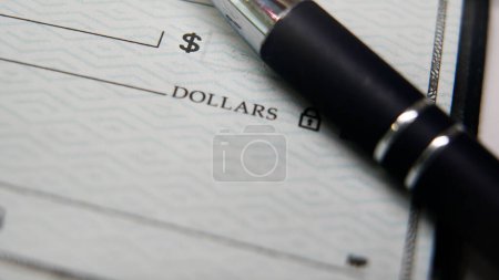 Ein blauer Stift steht auf einem Blankoscheck, dessen Spitze in der Nähe der Zahlungszeile ruht, bereit für jemanden, der die notwendigen Details für eine Finanztransaktion ausfüllt..