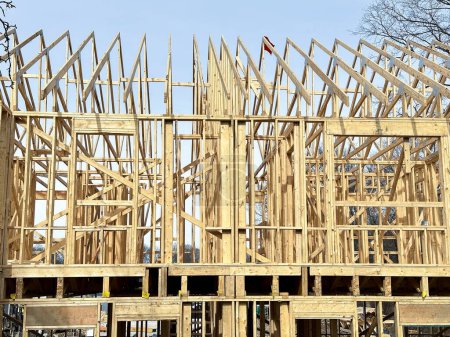 The skeleton of a new house stands with wooden beams and frames outlining the structure.