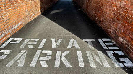 Private parking text on asphalt walkway between brick walls