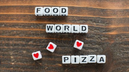 Diversos dados de carta ingeniosamente dispuestos para deletrear el mensaje Food Loves World Pizza contra la rica textura de un fondo de madera
