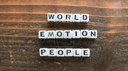 Cuentas de letras en cubos con letras negras deletrean las palabras Mundo, emoción y gente en una superficie rústica de madera que sugiere un tema de sentimiento global y conexiones humanas.