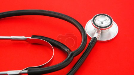 A stethoscope, indicative of the medical profession, is laid out on a pristine red background
