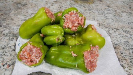 Several green bell peppers, with tops cut off and seeds removed, are filled with a mixture of raw ground meat, presumably for cooking.