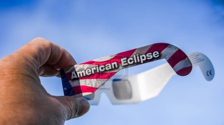 Foto de NORWALK, CT, Estados Unidos - 8 de ABRIL de 2024: Se muestra una mano sosteniendo un eclipse de gafas con Eclipse Americano impreso en ellas, adornado con el diseño de la bandera de Estados Unidos - Imagen libre de derechos