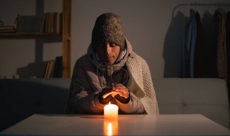 Photo for Young man without electricity at home with candle. Shutdown of heating and electricity, power outage, blackout, load shedding or energy crisis. copy space. - Royalty Free Image