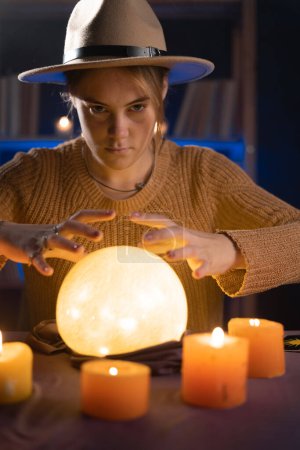 Photo for Soothsayer using crystal ball to predict future at table in darkness with candles. Fortune telling concept - Royalty Free Image
