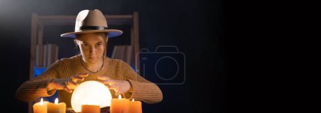 Photo for Soothsayer using crystal ball to predict future at table in darkness with candles. Fortune telling concept. Banner - Royalty Free Image