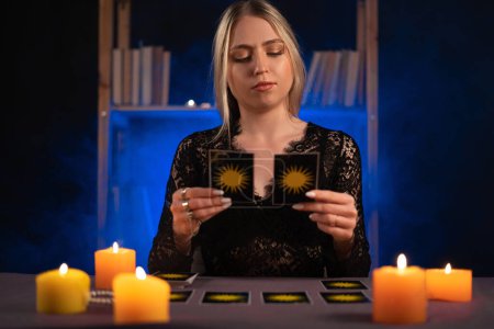 Photo for Fortune teller of hands holding tarot cards on table near burning candles in candle light.Tarot cards spread on table. Forecasting concept. - Royalty Free Image
