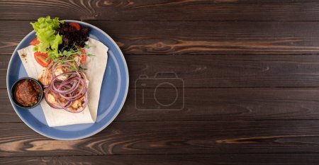 Foto de Kebab con salsa y verduras en un plato sobre un fondo de madera, vista superior. Vista superior - Imagen libre de derechos