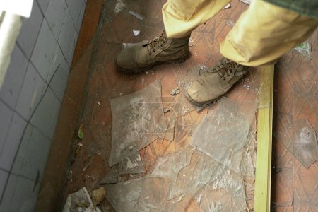 Téléchargez les photos : Gros plan des jambes dans de vieilles chaussures militaires sur des éclats de verre. espace de copie. - en image libre de droit