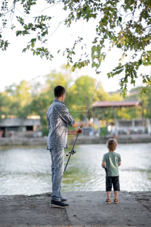 Téléchargez les photos : A rear view of father with a small toddler son outdoors fishing by a lake on pier. Copy space - en image libre de droit