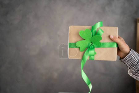 Hand of a young man holding a gift box with green ribbon on a gray background. Present for St.Patricks day concept