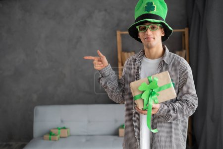 Photo for Funny happy excited man in leprechauns hat looking at camera showing pointing finger aside advertising St.Patrick's day promotion, St.Patrick's day discount ad on gray background. Copy space - Royalty Free Image