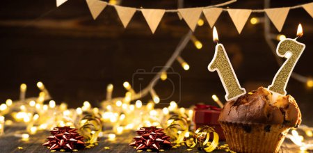 Photo for Number 17 gold burning candle in a cupcake against celebration wooden background with lights. Birthday cupcake. Copy space. Banner - Royalty Free Image