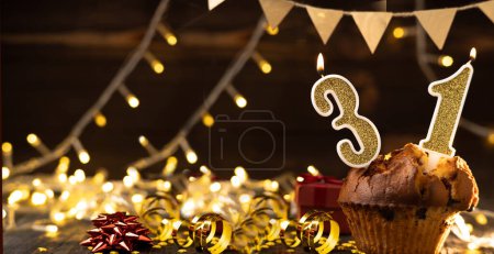 Photo for Number 31 gold burning candle in a cupcake against celebration wooden background with lights. Birthday cupcake. Copy space. Banner - Royalty Free Image