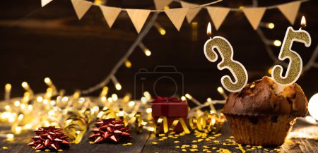 Téléchargez les photos : Number 35 birthday celebration candle in cupcake against lights and wooden background. Copy space. Banner - en image libre de droit