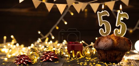 Foto de Number 55 golden festive burning candles in a cake, wooden holiday background. fifty-five years since the birth. the concept of celebrating a birthday, anniversary, holiday. Banner. copy space - Imagen libre de derechos