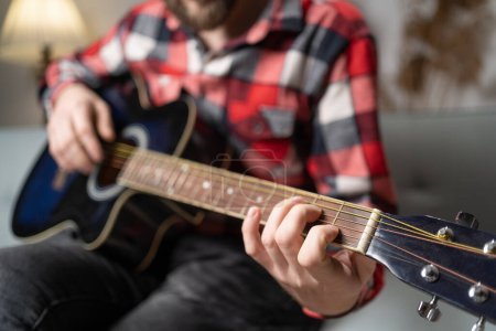 Photo for Male musician playing acoustic guitar on sofa at home. Copy space - Royalty Free Image