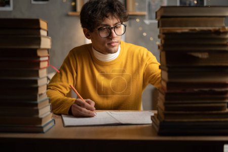 Young man college student writing with pen sitting near books. Copy space
