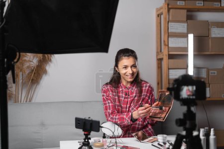 Young woman showing a makeup palette and brush on camera and recording video. Woman making a video for her beauty video blog on cosmetics. Copy space
