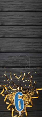 Téléchargez les photos : Number 6 blue celebration candle and gold confetti on dark wooden background. 6th birthday card. Anniversary and birthday concept. Vertical banner. Copy space - en image libre de droit