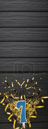 Téléchargez les photos : Number 7 blue celebration candle and gold confetti on dark wooden background. 7th birthday card. Anniversary and birthday concept. Vertical banner. Copy space - en image libre de droit