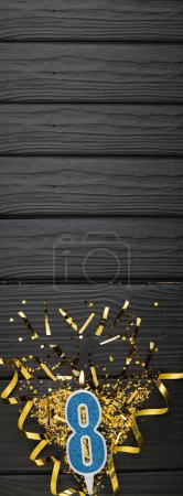 Téléchargez les photos : Number 8 blue celebration candle and gold confetti on dark wooden background. 8th birthday card. Anniversary and birthday concept. Vertical banner. Copy space - en image libre de droit