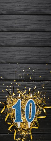 Téléchargez les photos : Number 10 blue celebration candle and gold confetti on dark wooden background. 10th birthday card. Anniversary and birthday concept. Vertical banner. Copy space - en image libre de droit