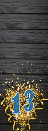 Téléchargez les photos : Number 13 blue celebration candle and gold confetti on dark wooden background. 13th birthday card. Anniversary and birthday concept. Vertical banner. Copy space - en image libre de droit
