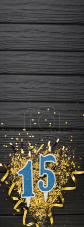Téléchargez les photos : Number 15 blue celebration candle and gold confetti on dark wooden background. 15th birthday card. Anniversary and birthday concept. Vertical banner. Copy space - en image libre de droit