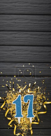 Téléchargez les photos : Number 17 blue celebration candle and gold confetti on dark wooden background. 17th birthday card. Anniversary and birthday concept. Vertical banner. Copy space - en image libre de droit