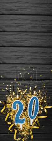 Téléchargez les photos : Number 20 blue celebration candle and gold confetti on dark wooden background. 20th birthday card. Anniversary and birthday concept. Vertical banner. Copy space - en image libre de droit