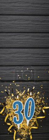 Téléchargez les photos : Number 30 blue celebration candle and gold confetti on dark wooden background. 30th birthday card. Anniversary and birthday concept. Vertical banner. Copy space - en image libre de droit