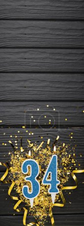 Foto de Vela de celebración azul número 34 y confeti dorado sobre fondo de madera oscura. Tarjeta de cumpleaños 34. Aniversario y concepto de cumpleaños. Banner vertical. Copiar espacio - Imagen libre de derechos