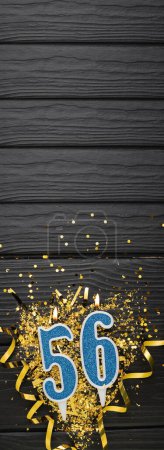 Photo for Number 56 blue celebration candle and gold confetti on dark wooden background. 56th birthday card. Anniversary and birthday concept. Vertical banner. Copy space - Royalty Free Image