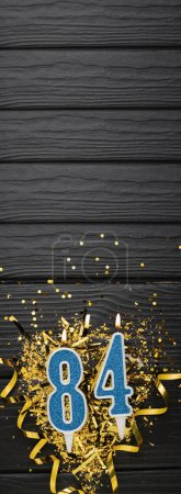 Photo for Number 84 blue celebration candle and gold confetti on dark wooden background. 84th birthday card. Anniversary and birthday concept. Vertical banner. Copy space - Royalty Free Image