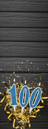 Vela de celebración azul número 100 y confeti dorado sobre fondo de madera oscura. Tarjeta de cumpleaños número 100. Aniversario y concepto de cumpleaños. Banner vertical. Copiar espacio