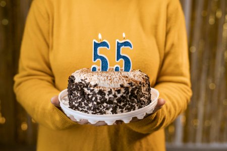 Foto de Mujer sosteniendo un pastel festivo con el número 55 velas mientras celebra la fiesta de cumpleaños. Concepto de fiesta de cumpleaños de la gente. Vista de primer plano - Imagen libre de derechos