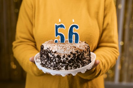 Photo for Woman holding a festive cake with number 56 candles while celebrating birthday party. Birthday holiday party people concept. Close-up view - Royalty Free Image