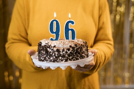 Foto de Feliz cumpleaños. Mujer sosteniendo pastel de cumpleaños delicioso fresco con vela encendida número 96, de cerca. Celebración del cumpleaños en casa. Copiar espacio - Imagen libre de derechos