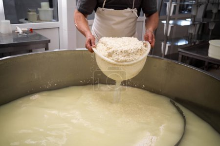 Téléchargez les photos : Fromagerie ou ouvrier qui prend la caillé du réservoir à la fromagerie, gros plan. Filtrage du lait de fermentation. Espace de copie - en image libre de droit