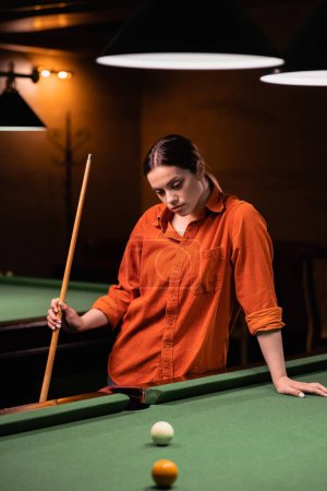Thoughtful young woman plays billiards. Billiard room on the background. Copy space