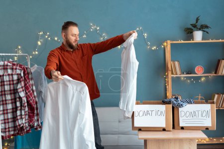 Photo for Man holding clothes and packing it in donate box in his room, Donation Concept. Copy space - Royalty Free Image