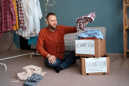 Téléchargez les photos : Don et concept de charité. Un homme emballant une boîte de dons avec des vêtements. Aider les pauvres et les nécessiteux. Espace de copie - en image libre de droit