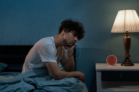 Téléchargez les photos : Jeune homme arabe déprimé assis dans son lit ne peut pas dormir de l'insomnie. Dépression et troubles du sommeil concept - en image libre de droit