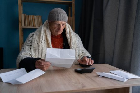 Freezing old man holding bills for electricity, gas and heating, calculating it. Global energy crisis concept. Cold home, Global energy crisis concept