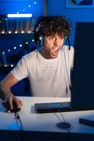 Photo for Young arabic gamer wearing headphones playing video game on personal computer, play in eSport cyber games tournament in neon light. Shocked screaming guy looking on monitor. Copy space - Royalty Free Image