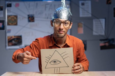 Téléchargez les photos : Étrange homme au chapeau en aluminium avec symbole maçonnique Œil de Dieu qui voit tout. Fausses nouvelles théorie du complot concept - en image libre de droit