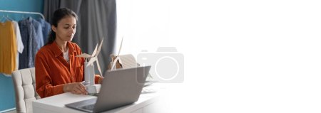 Foto de Ingeniero de ecología sentado en casa haciendo modelos de molino de viento y utilizando el ordenador portátil. Concepto de desarrollo sostenible. Banner. Copiar espacio - Imagen libre de derechos
